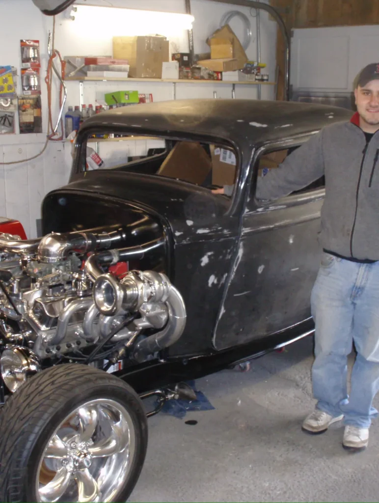 Chris at 19 standing beside his twin-turbo coupe in the family garage